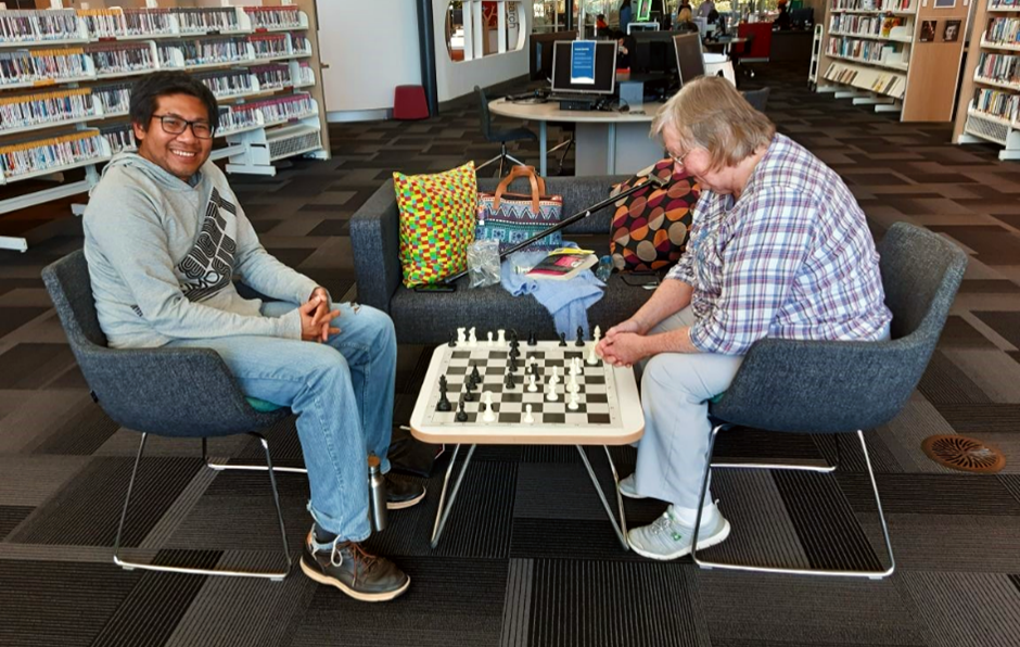 man and woman playing chess together in a library